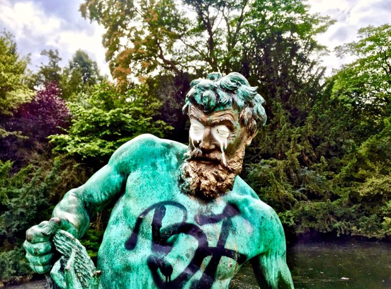 A imagem mostra a escultura de um homem, toda vandalizada e pixada, como um Atlas que já está cansado de ser explorado e não reconhecido.