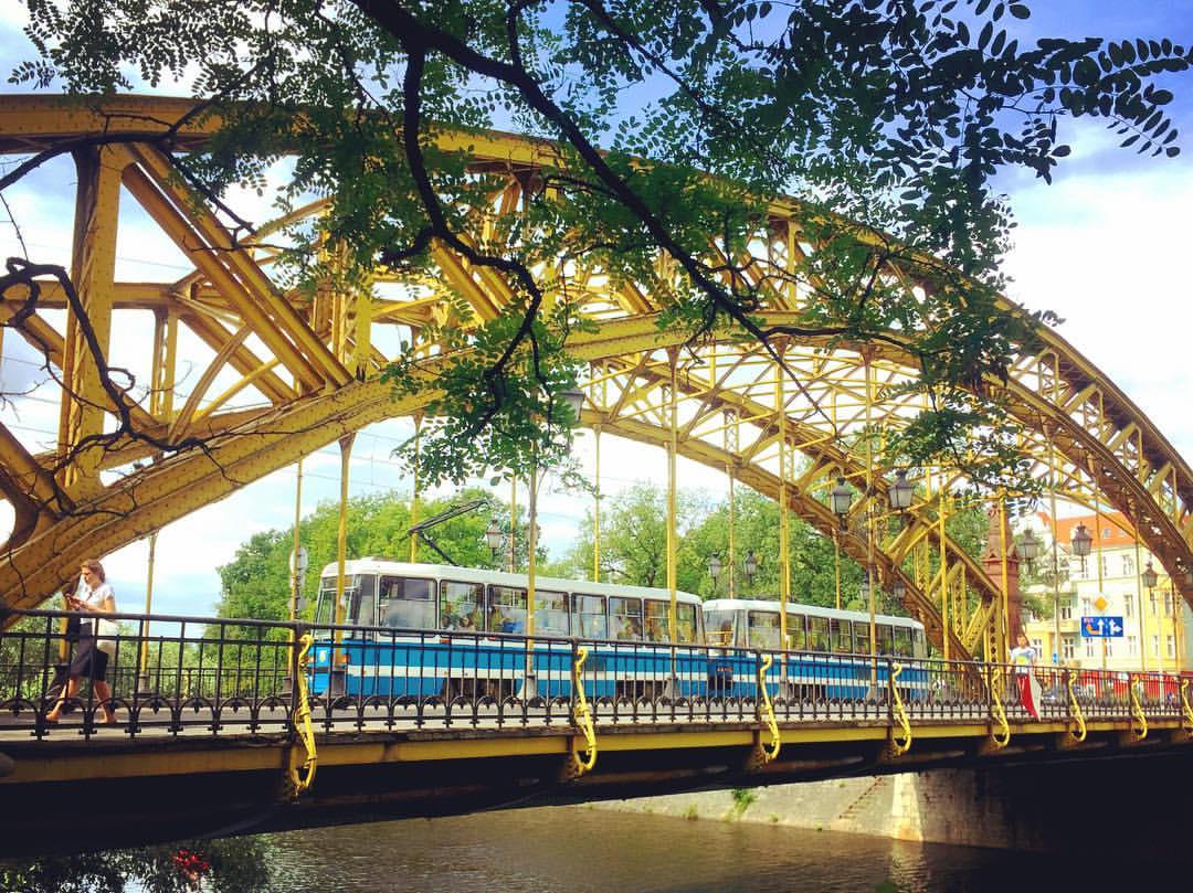 #paracegover Descrição para deficientes visuais: a imagem mostra um tram azul de modelo bem antigo atravessando uma linda ponte amarela de ferro. — at Zwierzyniecki Bridge.