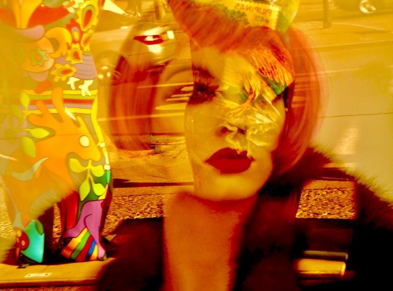 A imagem mostra uma manequim ruiva exposta numa vitrine. Reflexos coloridos compõem a cena.