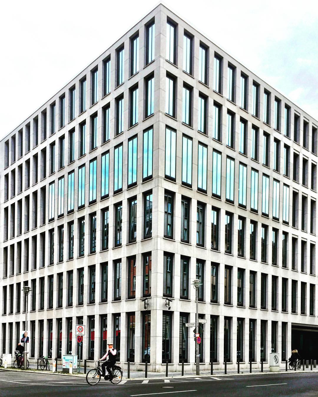 7. Adoro paisagens simétricas! E você? #paracegover A imagem mostra um prédio de concreto e vidro visto de esquina, em perfeita simetria. No canto esquerdo, passa um ciclista ( Französische Straße).
