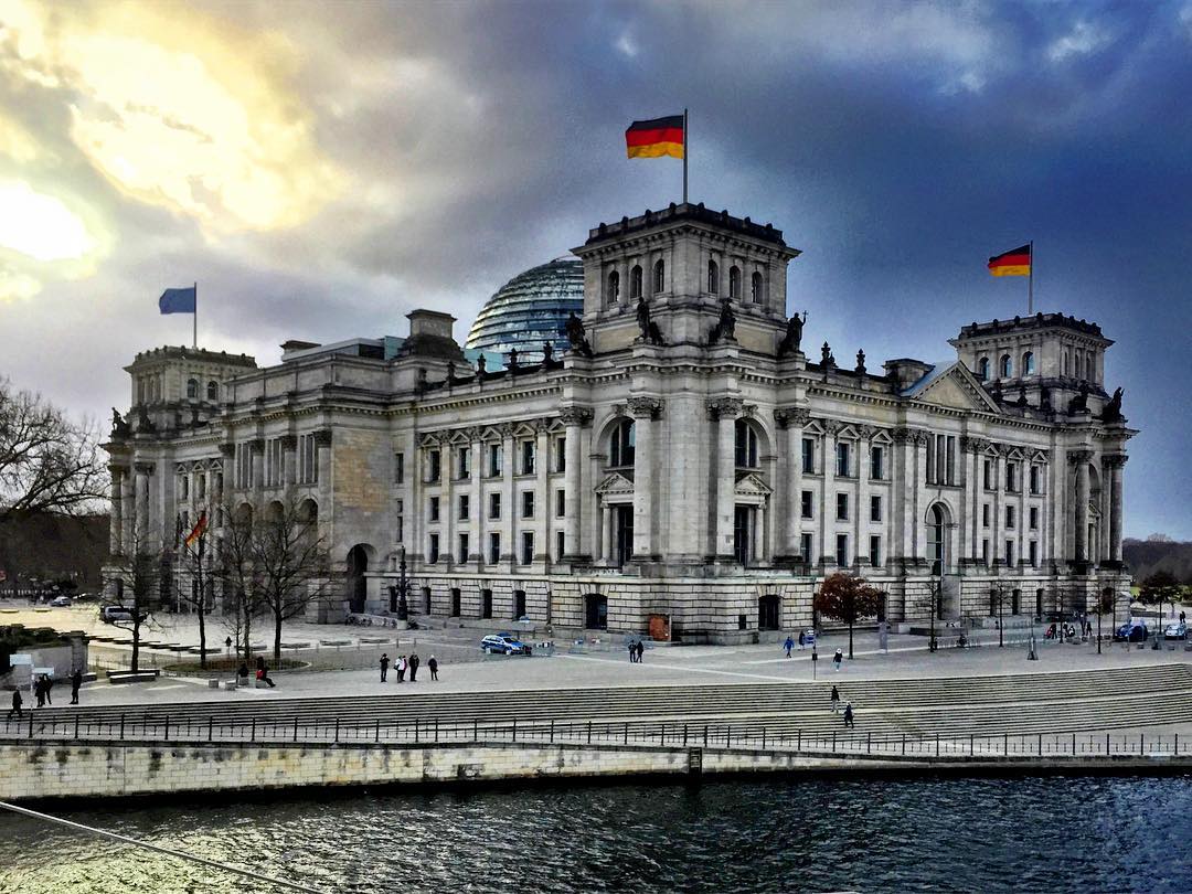 1. O parlamento alemão, com toda sua beleza! #paracegover A imagem mostra o prédio do Parlamento Alemão à beira do rio Spree. O céu está dramático. — at Berlin, Reichstag.