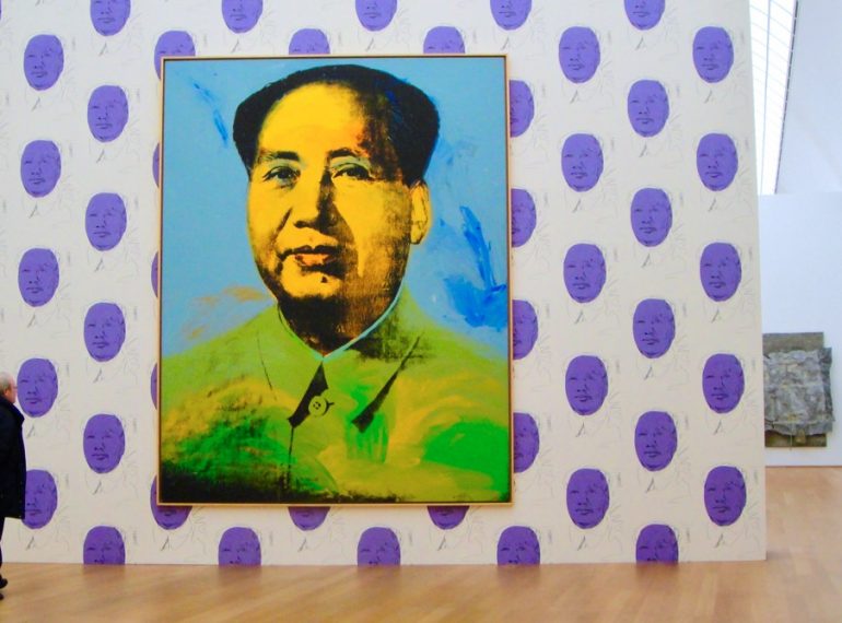 #paracegover A imagem mostra uma tela gigante de Andy Warhol exposta do Hamburger Bahnhof Museum, em Berlim, com um retrato de Mao Tse Tung no centro em uma parede branca estampada com grandes bolas da cor lilás.