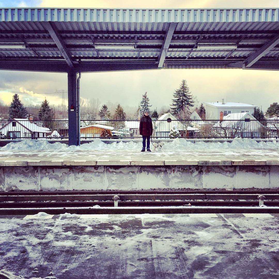  Descrição para deficientes visuais: a imagem mostra a estação de metrô Biesdorf-Süd toda cercada por neve, exceto por um homem e seu cachorro branco. — in Biesdorf Süd, Berlin, Germany.
