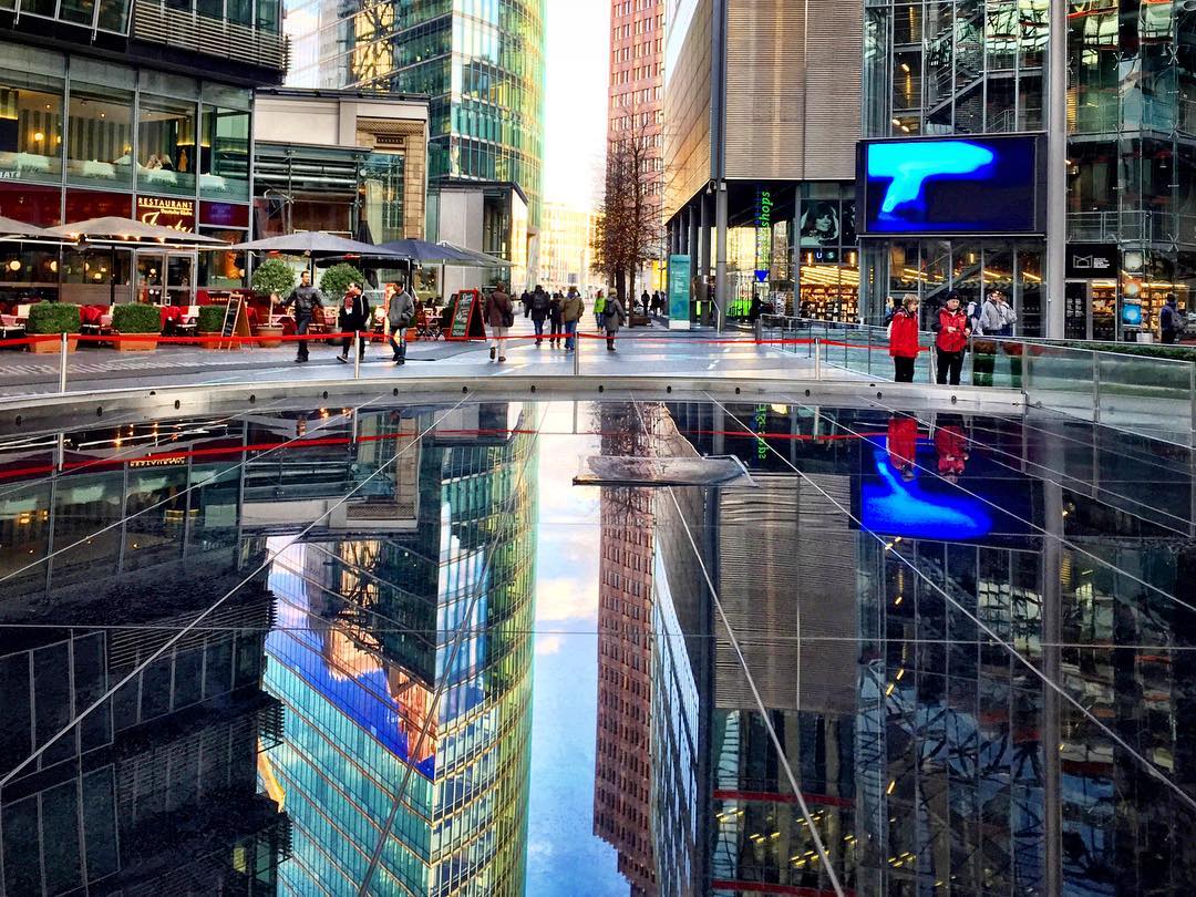 #paracegover Descrição para deficientes visuais: a imagem mostra a praça central do Sony Center, em Berlim. O piso de granito preto reflete a arquitetura desenhada em concreto, aço e muito vidro. — at Sony Center.