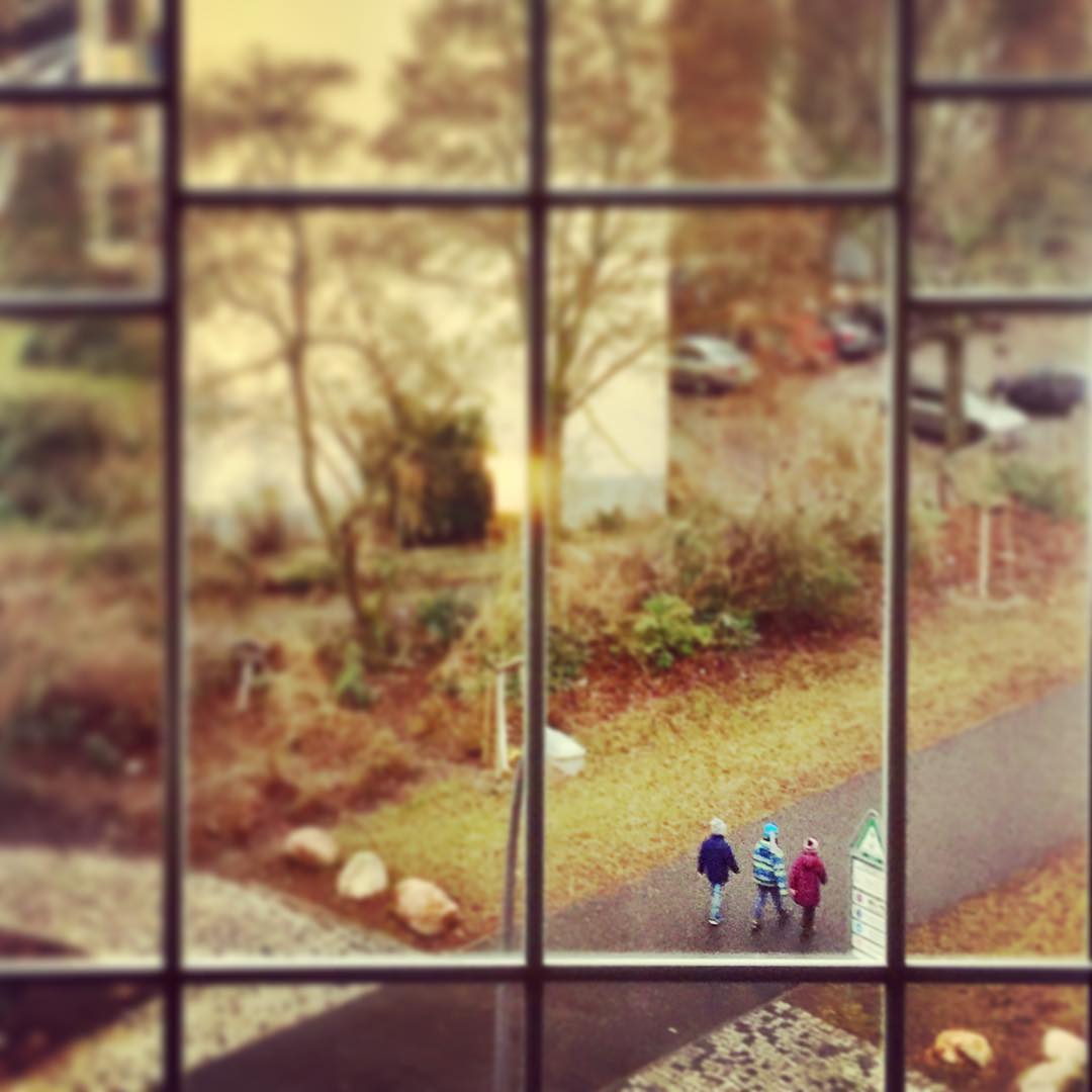 #paracegover Descrição para deficientes visuais: a imagem mostra três crianças caminhando em uma rua ao lado de uma praça. A cena é vista através das esquadrias de uma janela. — in Schöneberg, Berlin, Germany.