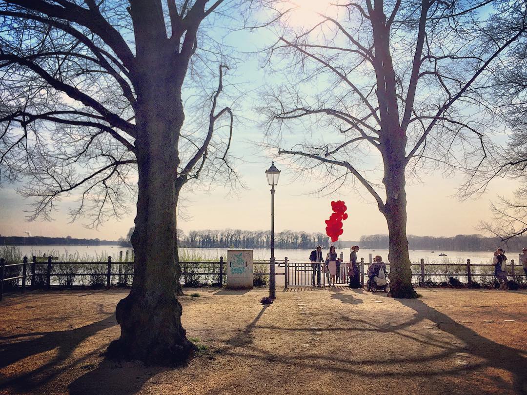 #paracegover Descrição para deficientes visuais: a imagem mostra um grupo de pessoas às margens do lago Tegel. A vegetação ainda está sem folhas. Uma das pessoas carrega um monte de balões vermelhos. Na verdade, acredito que estavam fotografando para uma campanha publicitária ou algo do gênero, a julgar pelo figurino do casal e o tamanho das lentes da fotógrafa 😊 — at Greenwichpromenade.