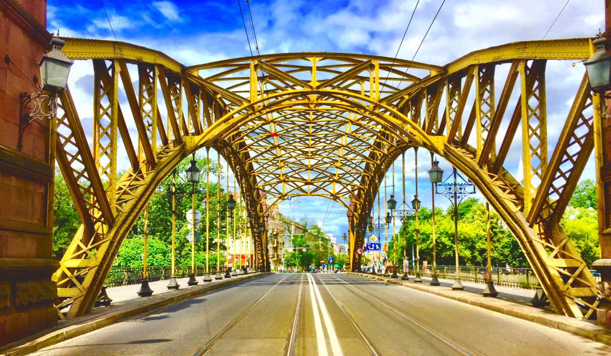 A imagem mostra uma ponte vista do vão central. Ela é de ferro e pintada de amarelo.