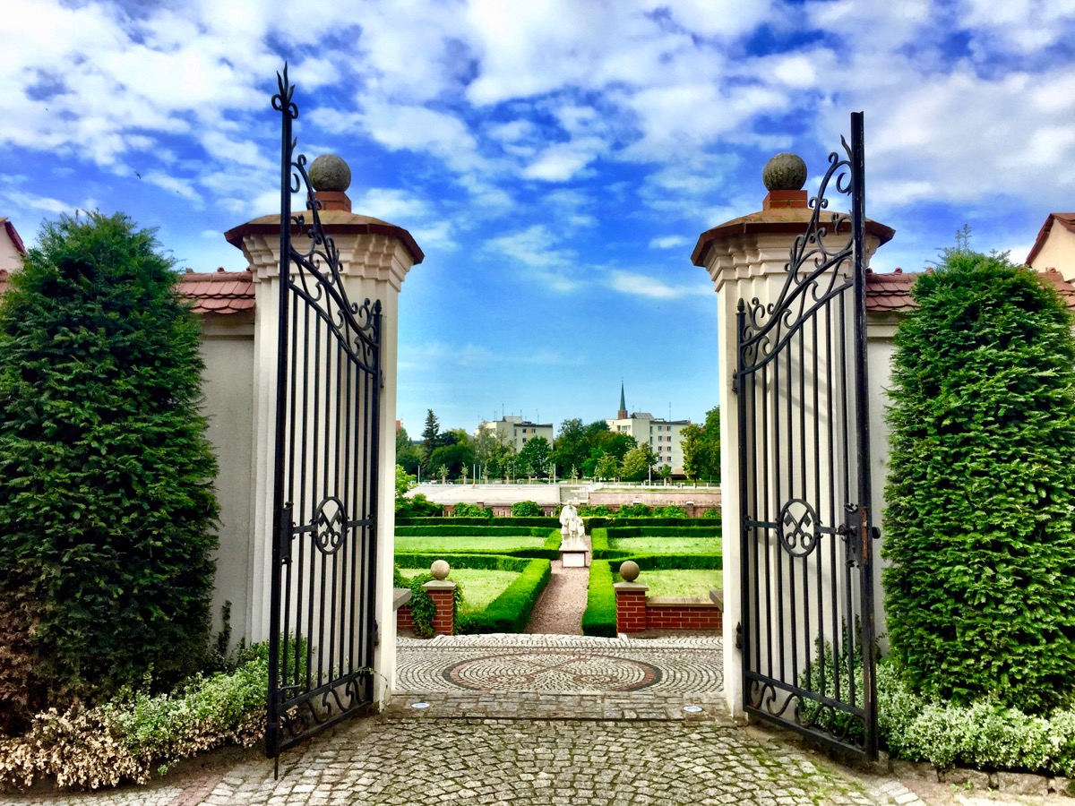 A imagem mostra um portão de entrada de um belíssimo e bem cuidado jardim.