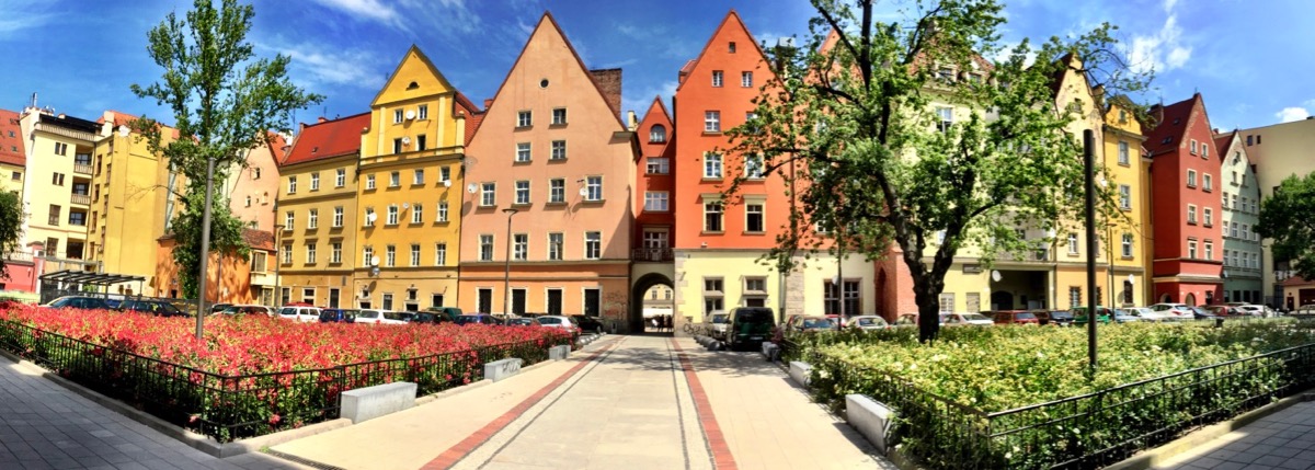 A imagem mostra uma visão panorâmica do casario de um pátio interno. As casas têm telhados triangulares e são pintadas de cores quentes.