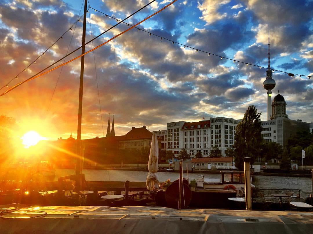 #paracegover Descrição para deficientes visuais: a imagem mostra o porto histórico coberto pela luz dourada do sol que se põe, quase 9 horas da noite. O céu ainda tem algumas nuvens, mas está limpando. — at Historischer Hafen Berlin.