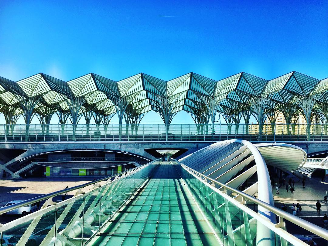 #paracegover Descrição para deficientes visuais: a imagem mostra uma vista da estação Gare do Oriente, com uma cobertura que parecem velas intercaladas num bordado maravilhoso. As curvas e retas são harmônicas; o vidro transparente refletindo o céu faz predominar a cor turquesa.