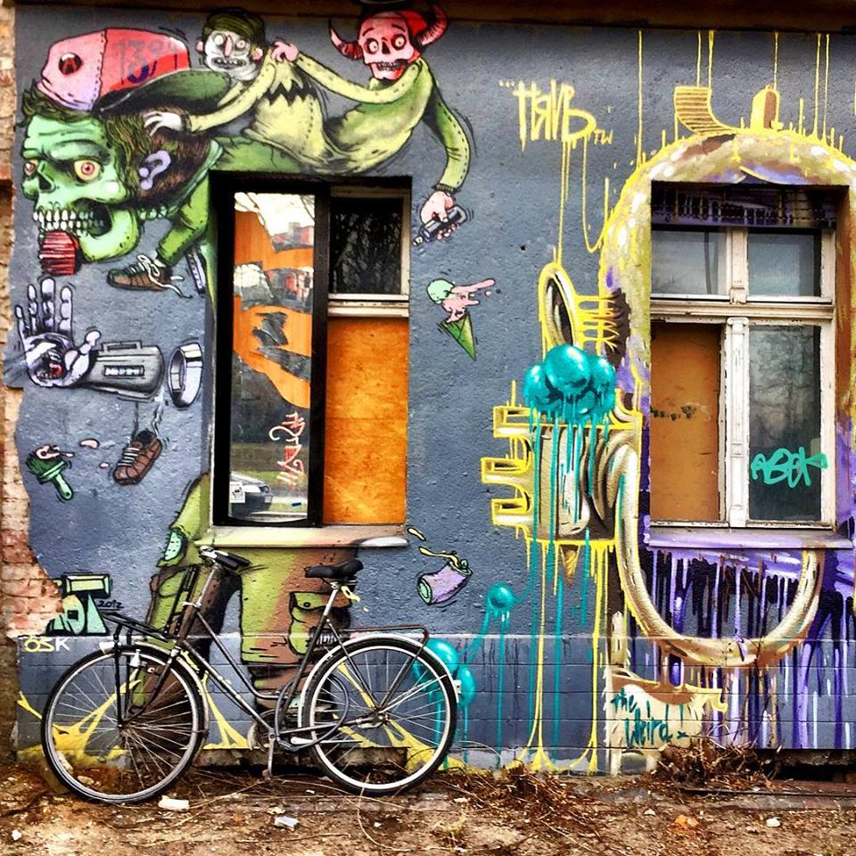 #paracegover Descrição para deficientes visuais: a imagem mostra uma bicicleta estacionada em frente a um prédio cuja fachada está toda grafitada com desenhos de criaturas fantásticas bem coloridas. — at nöldnerstraße.