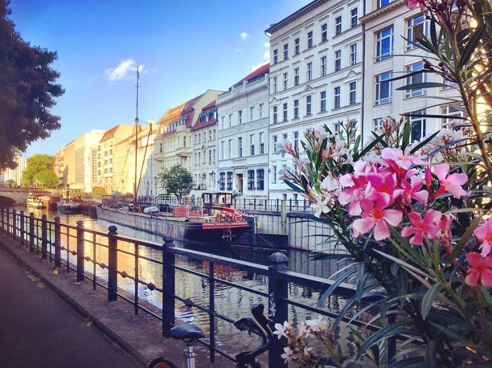 #paracegover Descrição para deficientes visuais: a imagem mostra um casario à beira de uma canal do rio Spree. Parte está na sombra, parte banhada pelo sol. Em primeiro plano, flores. — at Verona Restaurant.