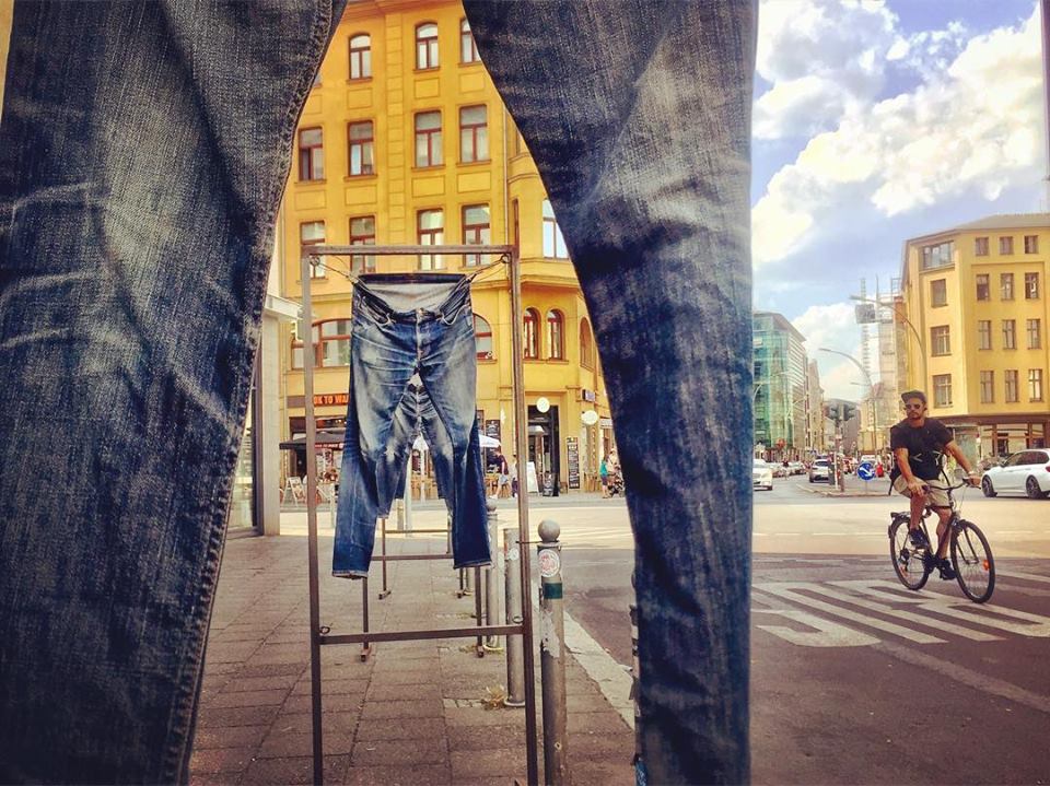 #paracegover Descrição para deficientes visuais: a imagem mostra uma instalação de calças jeans expostas na calçada em frente à loja da Levis. O ponto de vista é por entre as pernas de uma calçada. É possível ver os outros pares de jeans e os prédios amarelos ao fundo. Uma bicicleta passa na rua, do lado direito. — at Buttenheim Levis Icon Store.