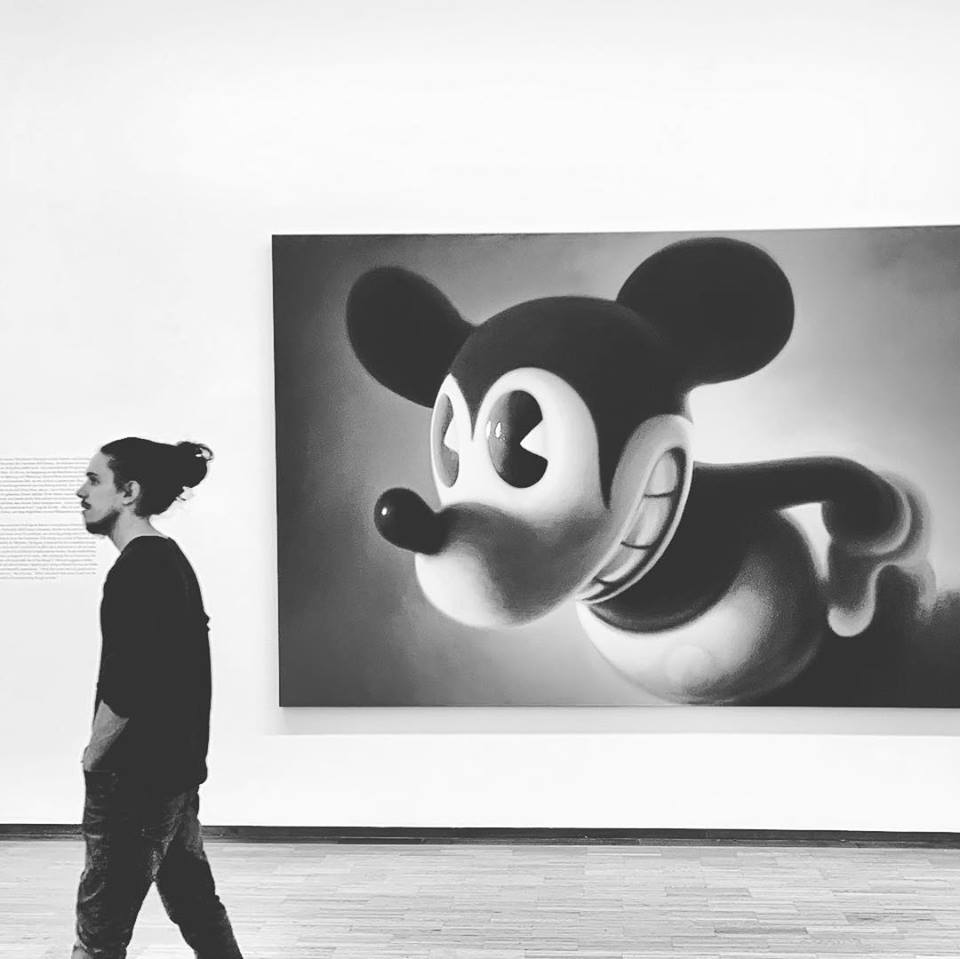 #paracegover Descrição para deficientes visuais: a imagem mostra a obra “Pink Mouse 2” do artista austríaco Gottfried Helnwein, onde um Mickey Mouse um tanto quanto sinistro (uma crítica aos desenhos animados pós Segunda Guerra) olha para o lado, justamente na hora em que está passando um rapaz de dreads amarrados em coque, visitante do museu. O quadro é em tons de pink, mas achei que a versão em preto e branco ficou com um contraste melhor. — at Albertina Museum.