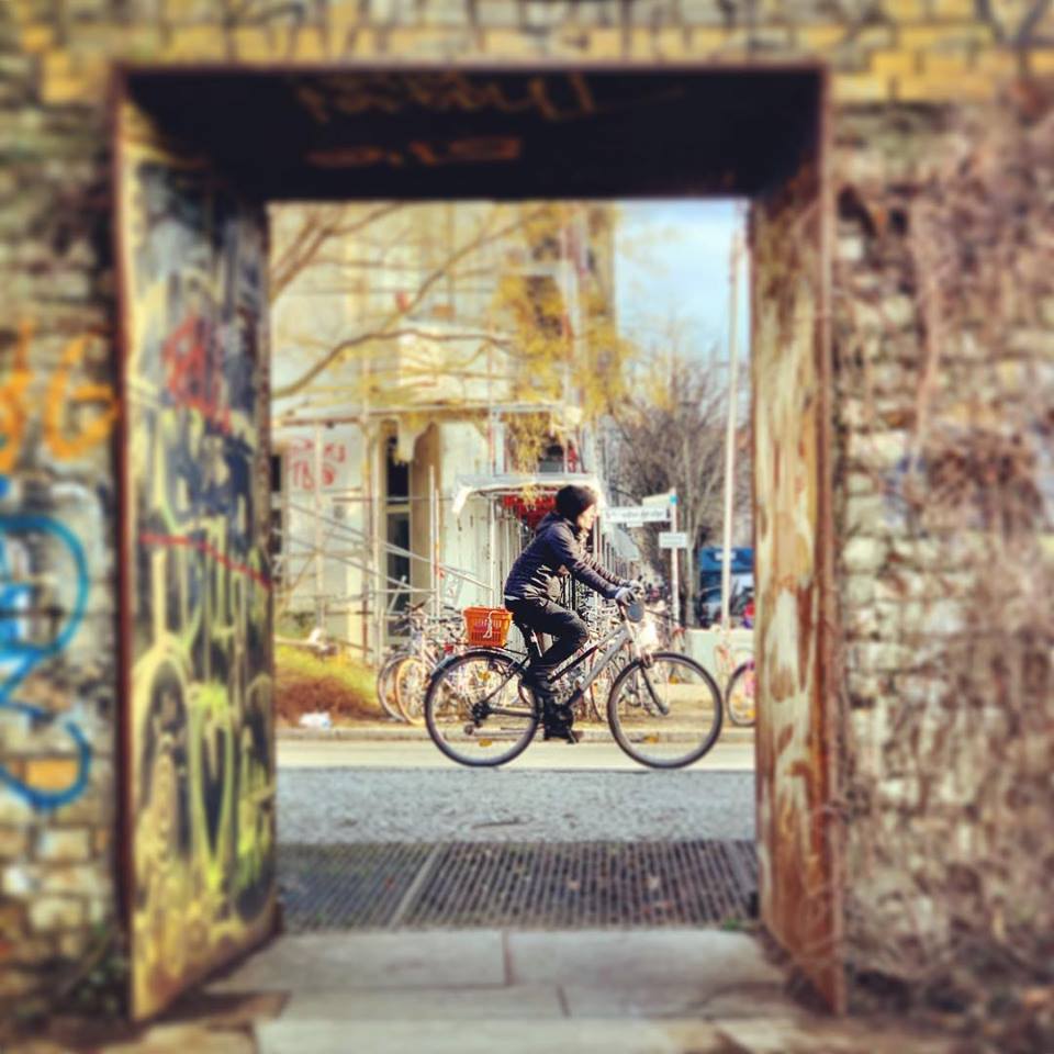 #paracegover Descrição para deficientes visuais: a imagem mostra um ciclista passando na rua visto de um portal. — at Schwedter Nordwand im Mauerpark.