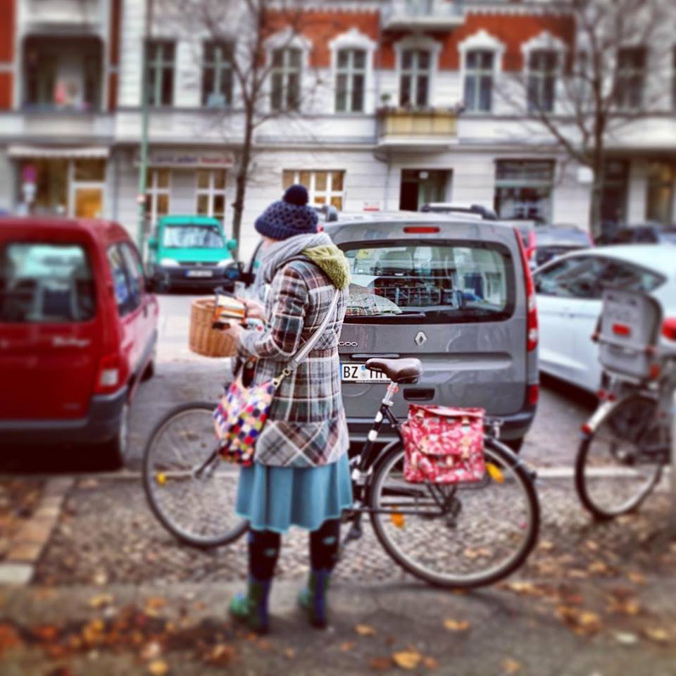#paracegover Descrição para deficientes visuais: a imagem mostra uma moça muito elegante cheia de cachecóis, touca, casacos e luvas preparando-se para sair com sua bicicleta. Mesmo com frio e tempo chuvoso, o povo aqui é muito valente! — in Prenzlauer Berg, Berlin, Germany.