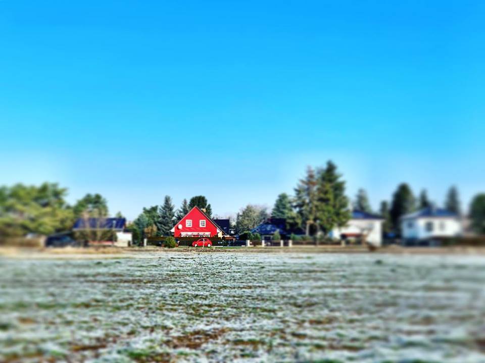 #paracegover Descrição para deficientes visuais: a imagem mostra um campo gramado coberto de gelo. Ao fundo, casas diversas; a que está em foco é um chalé vermelho com um carro da mesma cor estacionado em frente. Nem sempre odeio carros...rsrs — in Mahlsdorf, Berlin, Germany.
